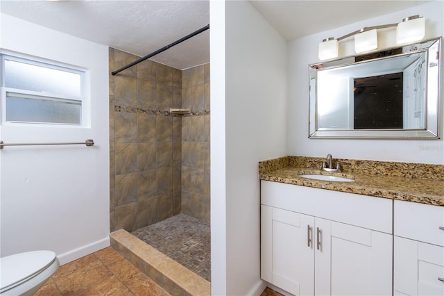 bathroom with baseboards, tiled shower, vanity, and toilet