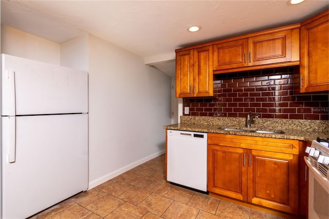 kitchen featuring white appliances, a sink, decorative backsplash, brown cabinets, and dark stone counters