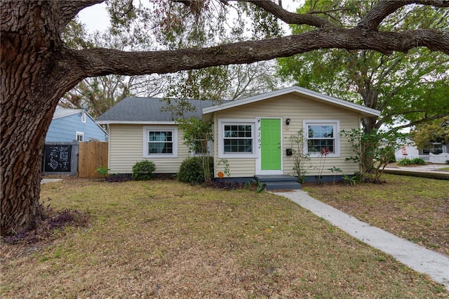 single story home with fence, a front lawn, and roof with shingles