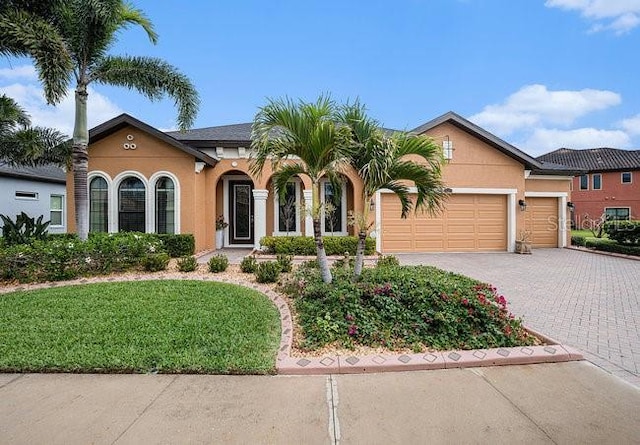 view of front facade with a front lawn, decorative driveway, an attached garage, and stucco siding