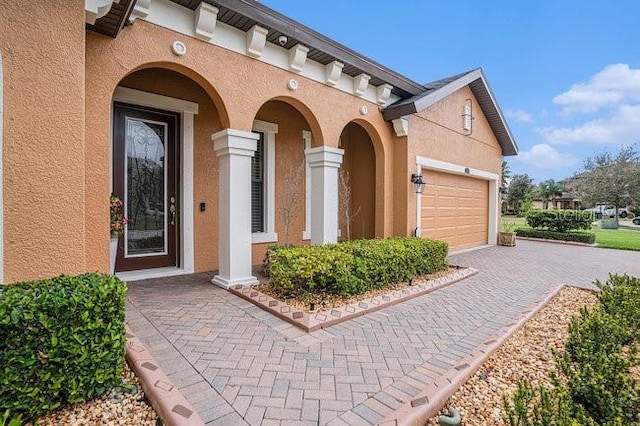 view of exterior entry with a garage, decorative driveway, and stucco siding