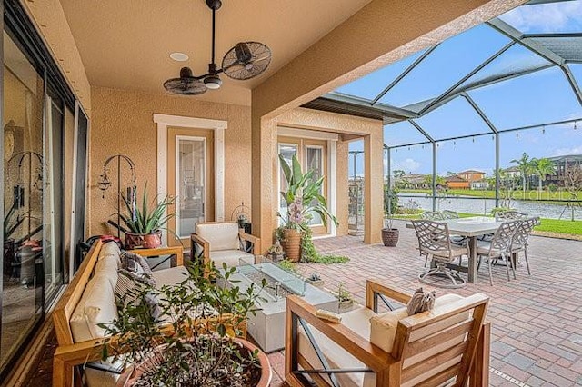 view of patio with a ceiling fan, outdoor dining space, a lanai, and a water view