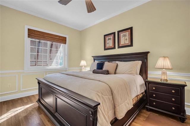 bedroom with dark wood-style floors, a decorative wall, ornamental molding, wainscoting, and ceiling fan