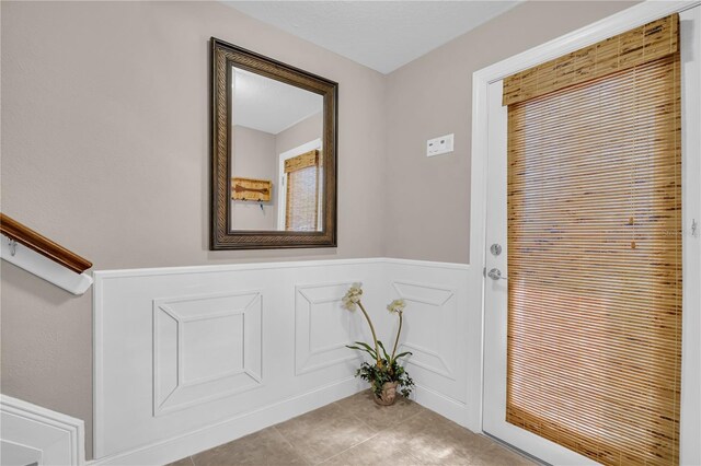 doorway featuring a wainscoted wall, a decorative wall, a textured ceiling, and tile patterned floors