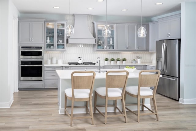 kitchen with gray cabinets, light countertops, custom range hood, backsplash, and appliances with stainless steel finishes