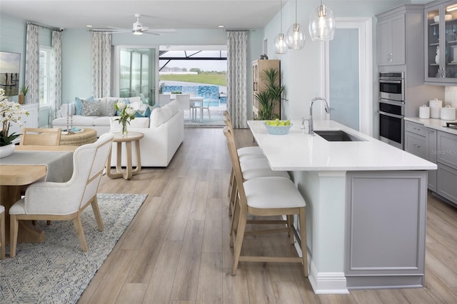 kitchen with stainless steel double oven, a sink, light countertops, gray cabinets, and light wood finished floors