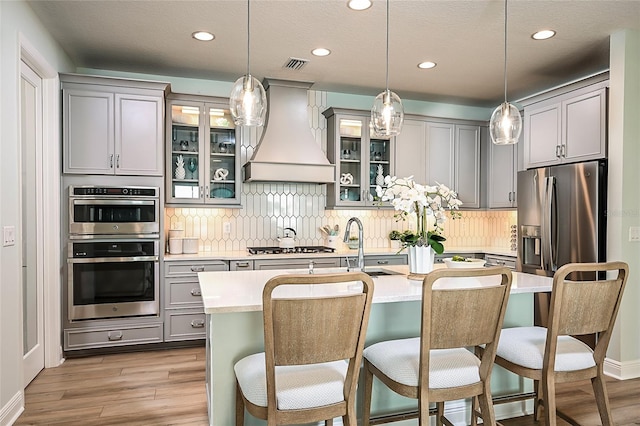 kitchen featuring stainless steel appliances, custom range hood, visible vents, backsplash, and gray cabinetry