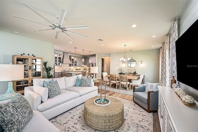 living room featuring ceiling fan with notable chandelier, light wood-type flooring, visible vents, and recessed lighting