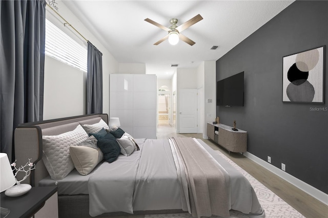 bedroom with ensuite bathroom, wood finished floors, a ceiling fan, visible vents, and baseboards