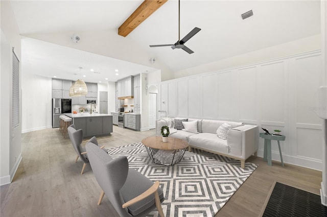 living area with light wood finished floors, visible vents, a decorative wall, ceiling fan, and beamed ceiling