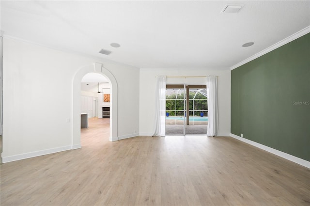 empty room featuring light wood-style floors, visible vents, crown molding, and baseboards