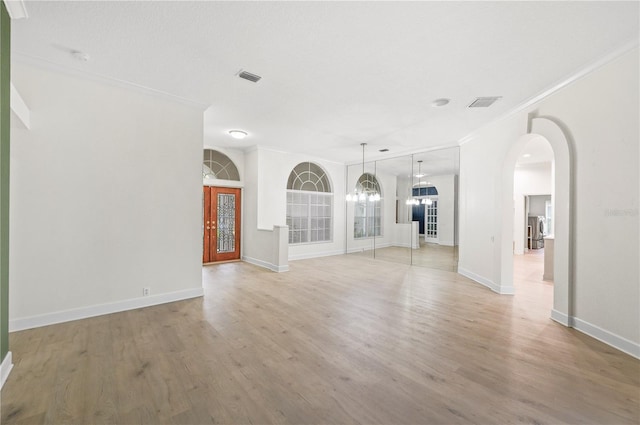 empty room featuring arched walkways, light wood finished floors, ornamental molding, and visible vents