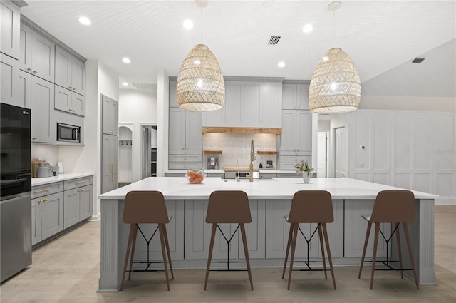 kitchen with arched walkways, gray cabinetry, light wood-style floors, appliances with stainless steel finishes, and backsplash