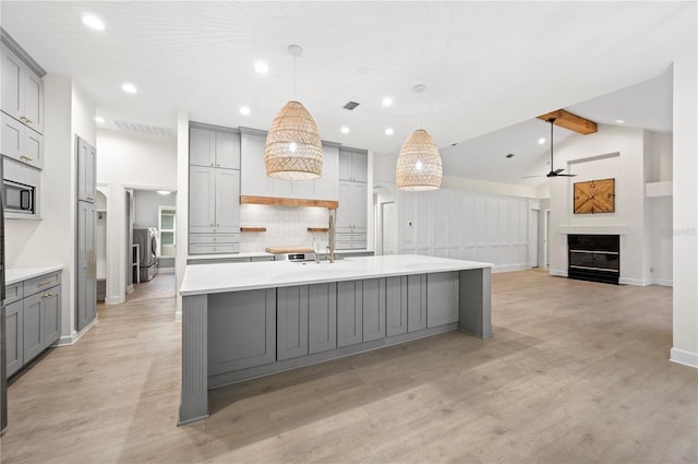 kitchen featuring light wood finished floors, gray cabinets, light countertops, and a glass covered fireplace