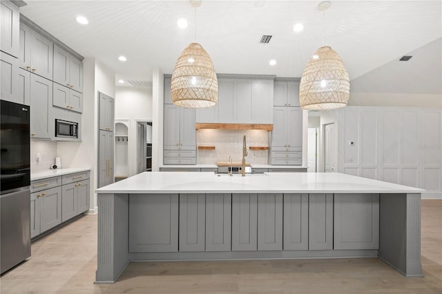 kitchen featuring arched walkways, decorative backsplash, appliances with stainless steel finishes, gray cabinets, and light wood-style floors