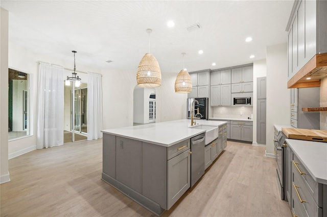 kitchen with stainless steel appliances, gray cabinets, light countertops, a sink, and light wood-type flooring