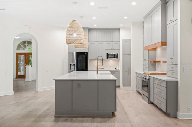 kitchen with stainless steel appliances, arched walkways, light countertops, and gray cabinetry