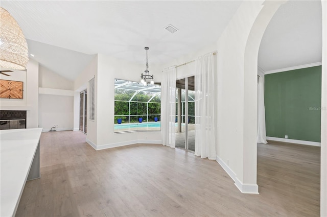 unfurnished dining area with light wood finished floors, baseboards, arched walkways, a glass covered fireplace, and a sunroom