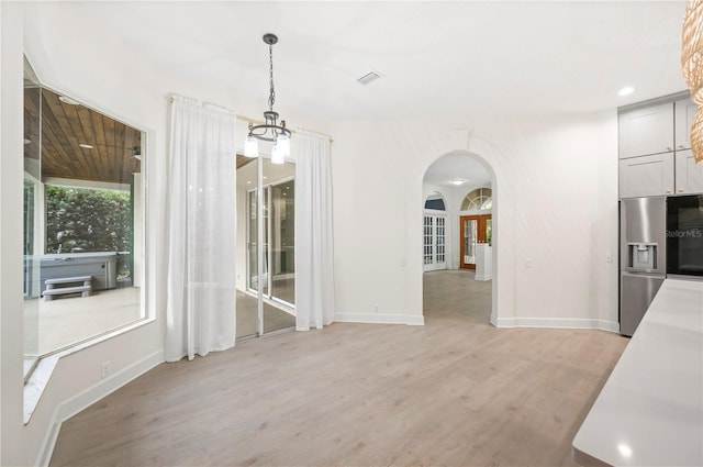 unfurnished dining area featuring arched walkways, a chandelier, light wood-style flooring, visible vents, and baseboards