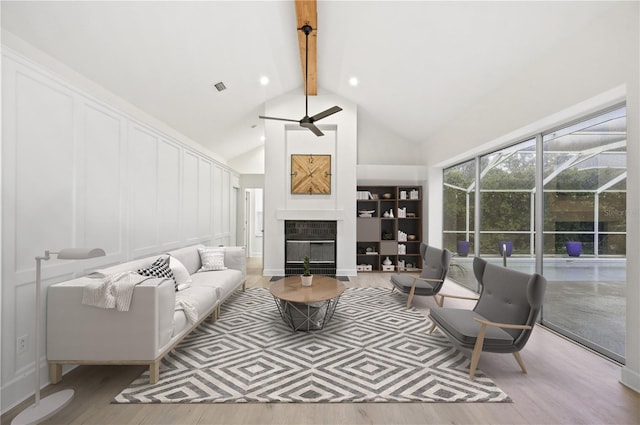 living room with beam ceiling, a fireplace, a decorative wall, a ceiling fan, and wood finished floors