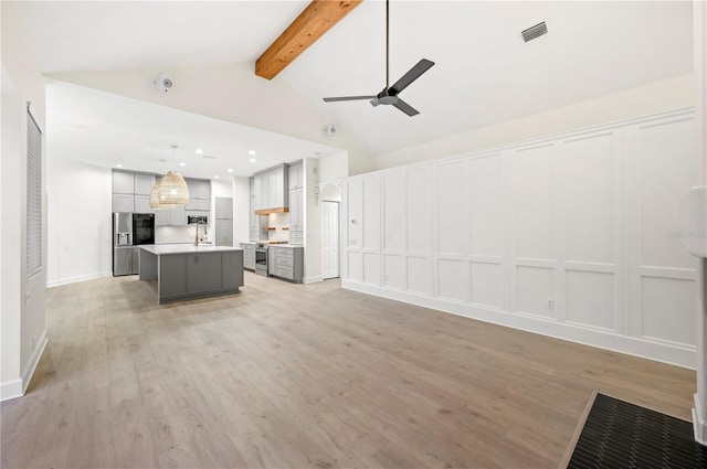 unfurnished living room with beam ceiling, visible vents, a decorative wall, a ceiling fan, and light wood-type flooring