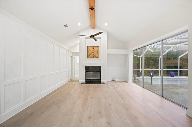 unfurnished living room with light wood finished floors, ceiling fan, a fireplace, a decorative wall, and beam ceiling