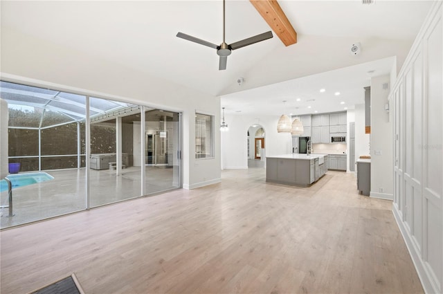 unfurnished living room with light wood finished floors, arched walkways, a ceiling fan, beamed ceiling, and high vaulted ceiling