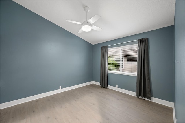 spare room featuring lofted ceiling, wood finished floors, a ceiling fan, and baseboards