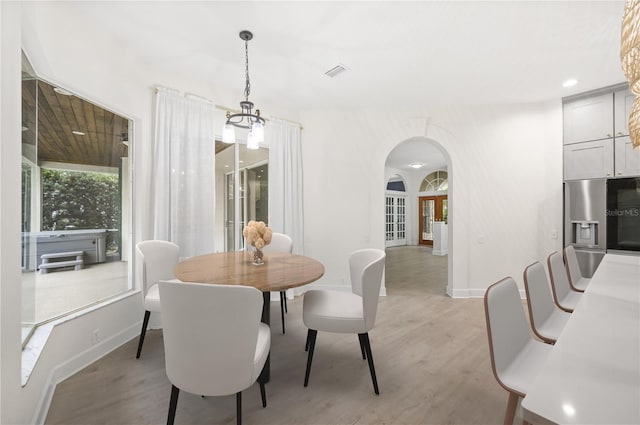 dining area with arched walkways, light wood finished floors, visible vents, and baseboards