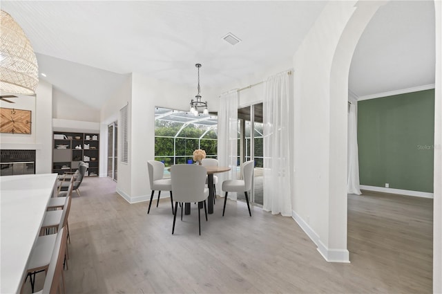 dining space featuring light wood-type flooring, baseboards, arched walkways, and a glass covered fireplace