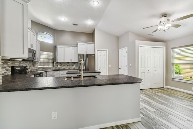 kitchen featuring electric stove, stainless steel fridge with ice dispenser, dark countertops, a peninsula, and a sink