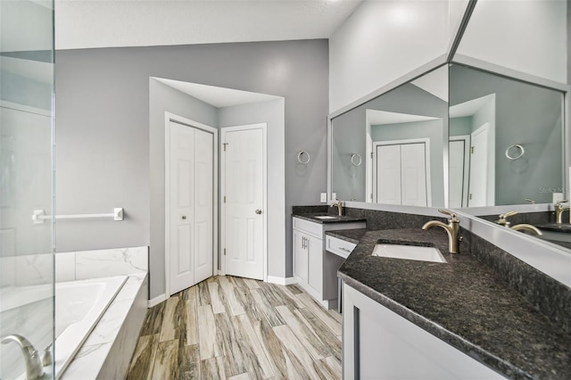 full bathroom with wood finished floors, a sink, vaulted ceiling, a closet, and tiled tub