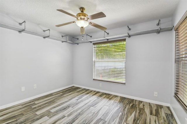 empty room with ceiling fan, a textured ceiling, baseboards, and wood finished floors