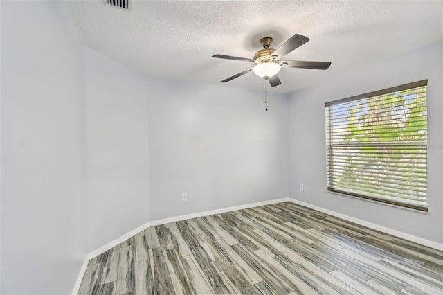 empty room with ceiling fan, a textured ceiling, baseboards, and wood finished floors