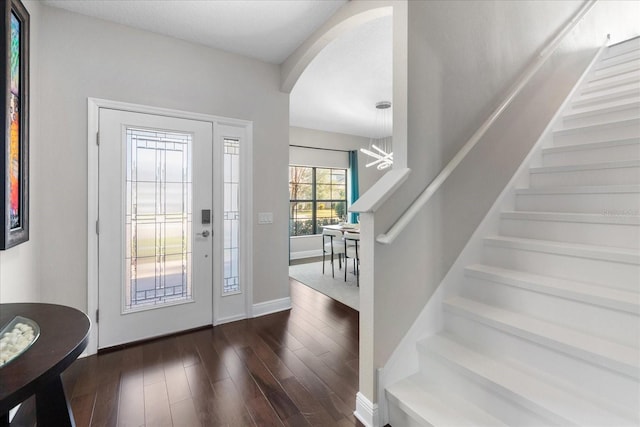 entrance foyer with baseboards, stairway, arched walkways, and dark wood-type flooring