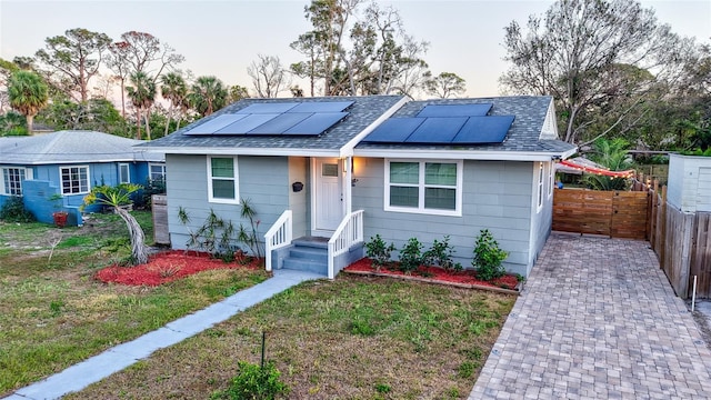 single story home featuring a shingled roof, fence, solar panels, and a front yard