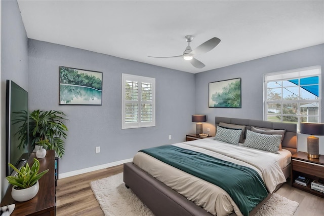 bedroom featuring multiple windows, ceiling fan, baseboards, and wood finished floors