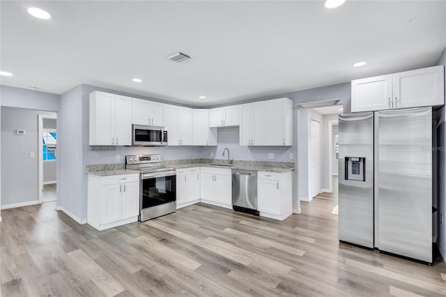 kitchen with light stone counters, light wood finished floors, stainless steel appliances, visible vents, and white cabinetry