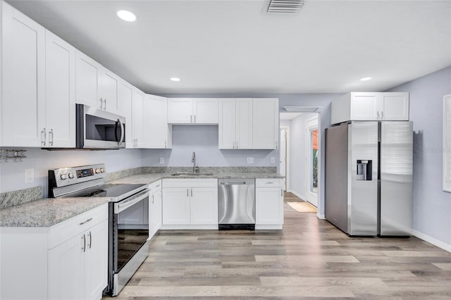 kitchen with stainless steel appliances, recessed lighting, white cabinets, a sink, and light wood-type flooring