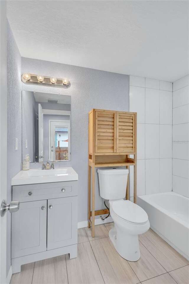 bathroom featuring a washtub, a textured wall, toilet, vanity, and baseboards