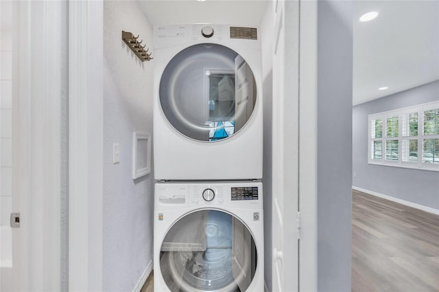 laundry area featuring laundry area, stacked washing maching and dryer, wood finished floors, and baseboards