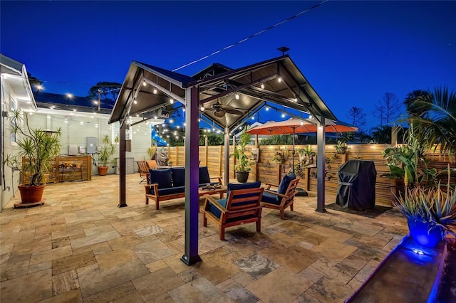 patio at twilight featuring ceiling fan, a fenced backyard, an outdoor hangout area, a grill, and a gazebo