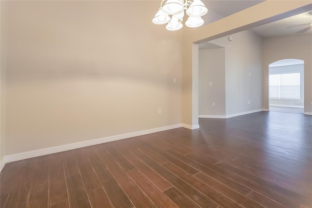 spare room with dark wood-style floors, baseboards, arched walkways, and a chandelier