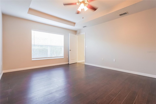 unfurnished room with a tray ceiling, dark wood-style flooring, and baseboards