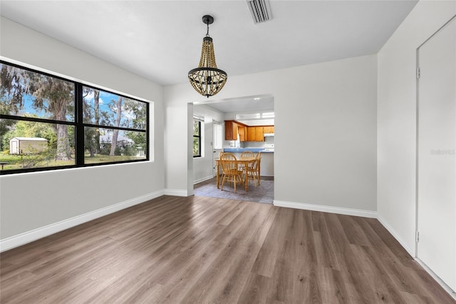 unfurnished living room with a chandelier, visible vents, baseboards, and wood finished floors