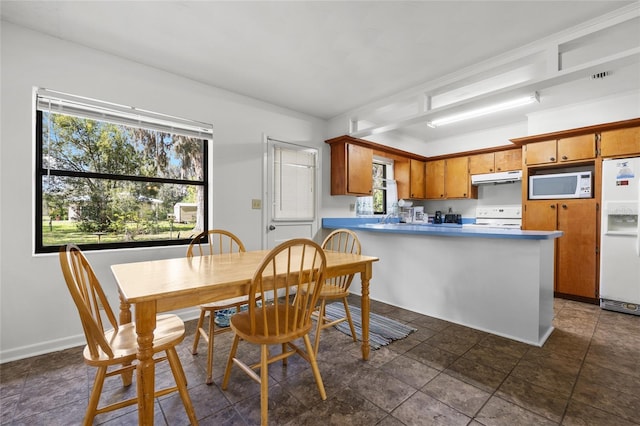 kitchen with a peninsula, white appliances, under cabinet range hood, and brown cabinets