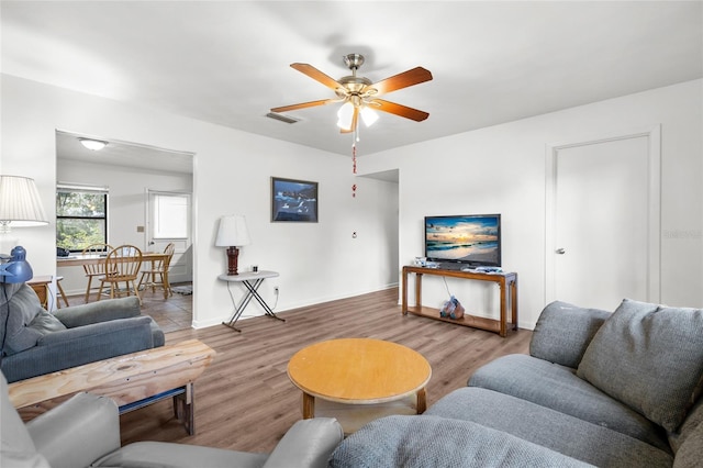 living area with ceiling fan, wood finished floors, visible vents, and baseboards