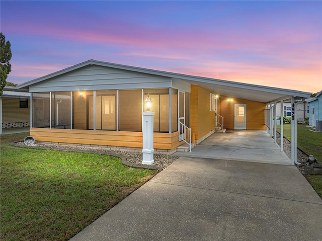 manufactured / mobile home featuring an attached carport, a sunroom, driveway, and a front lawn