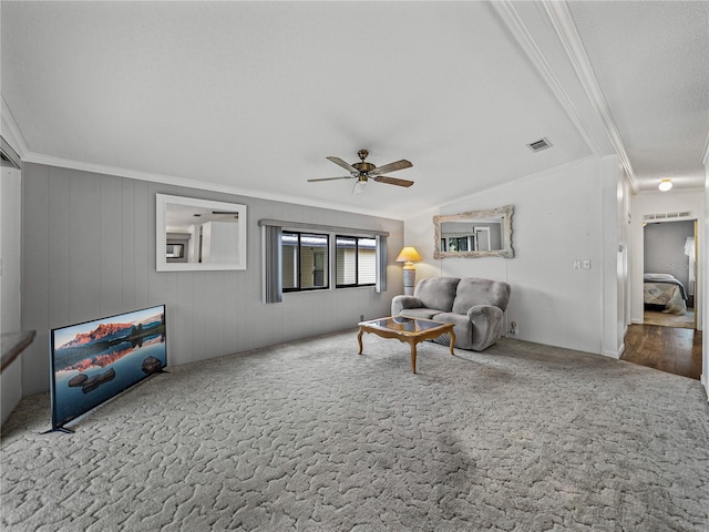 living area with ceiling fan, visible vents, carpet flooring, and ornamental molding