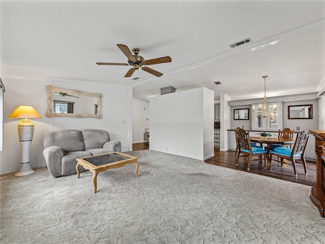 living room with ceiling fan with notable chandelier, wood finished floors, visible vents, ornamental molding, and plenty of natural light